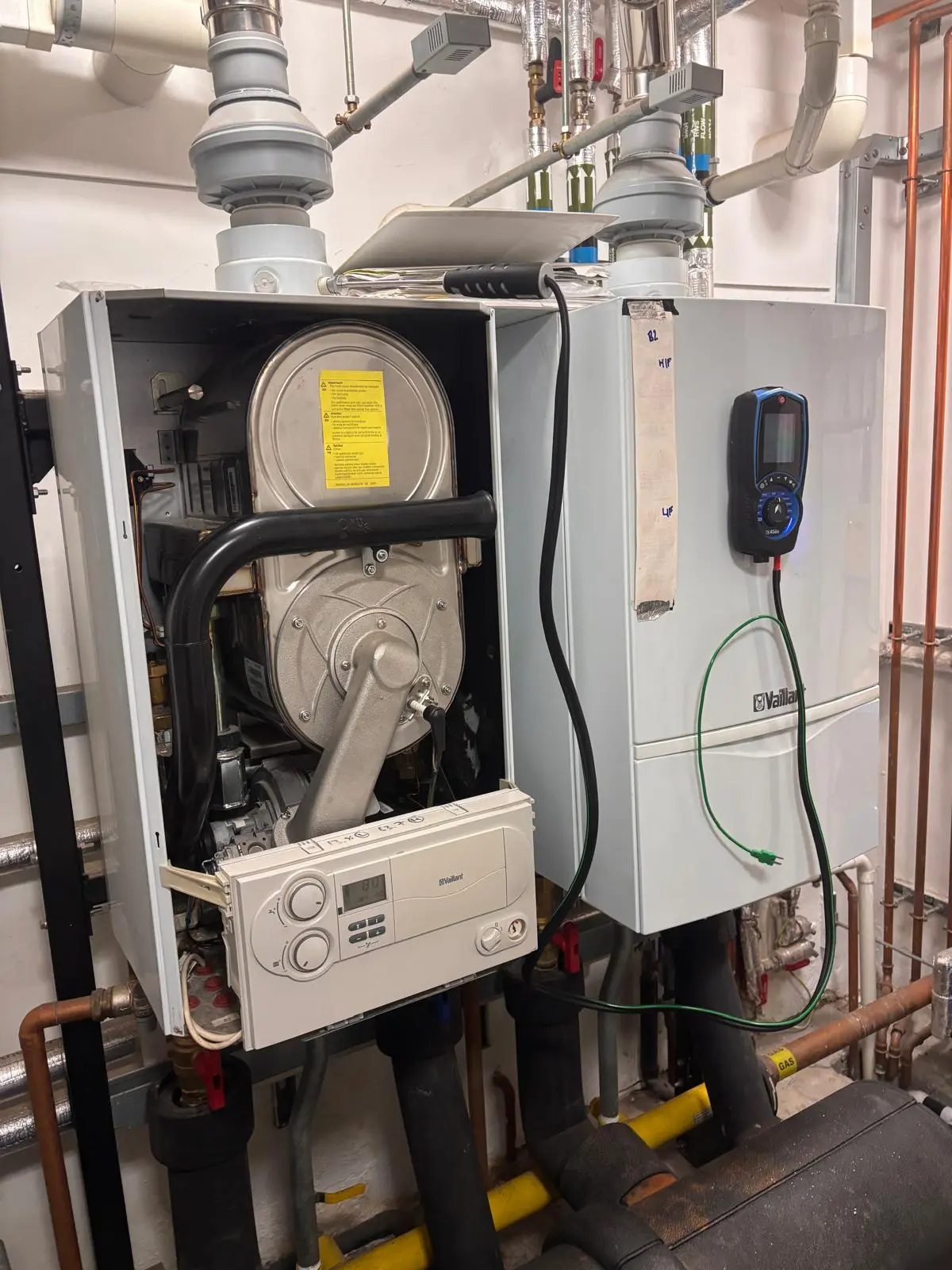 Two Vaillant commercial boilers in a plant room in Holland Park, London, one with the casing open and a gas analyser connected during a commercial gas safety inspection