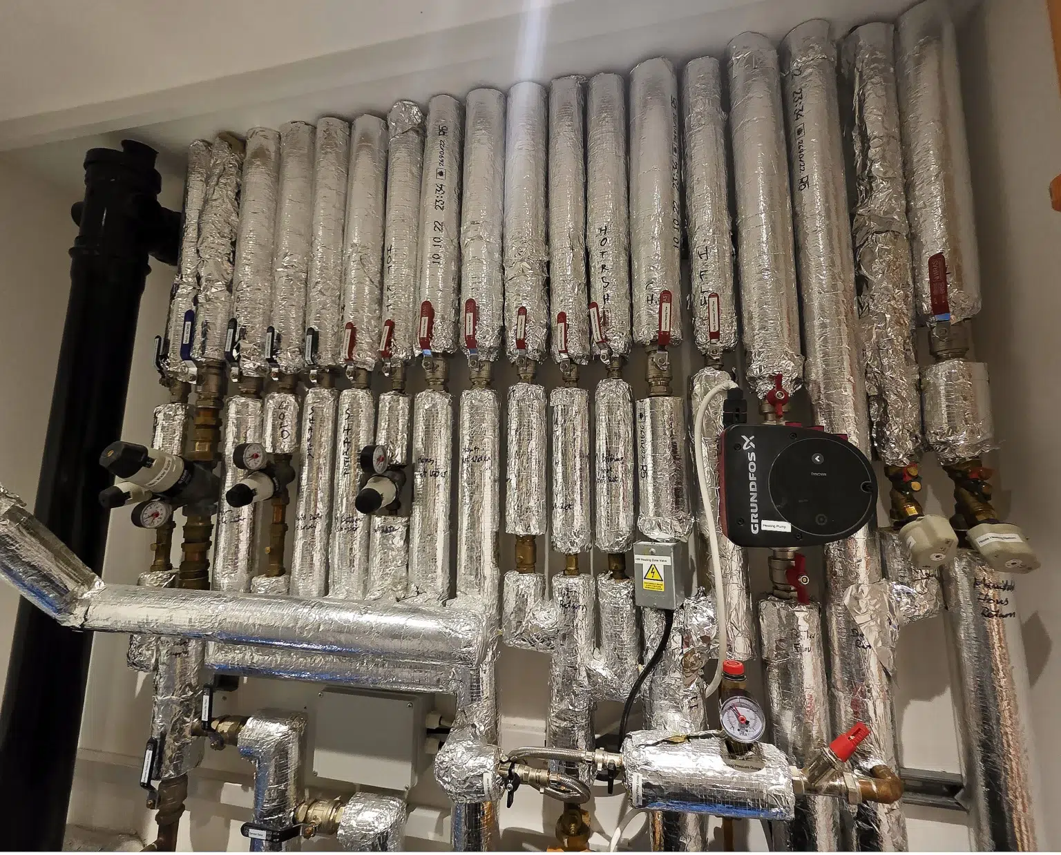 Commercial plant room in West London with insulated heating and hot water pipework, valves, pressure gauges and circulation pump